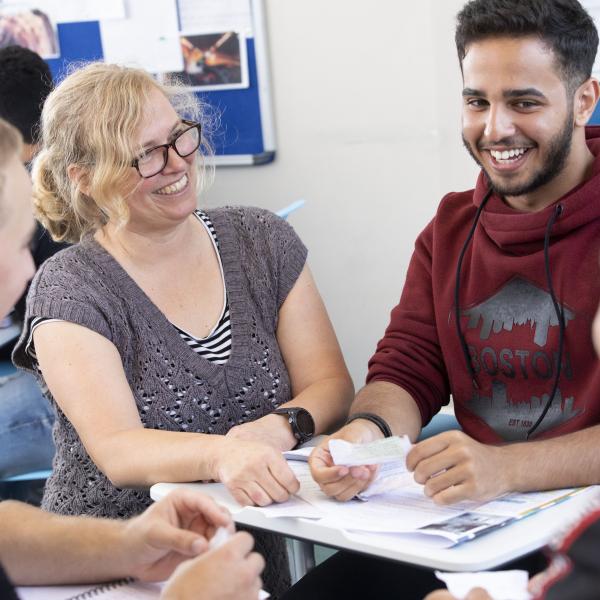 Student reading from a slip of paper, laughing, whilst being supported by the teacher